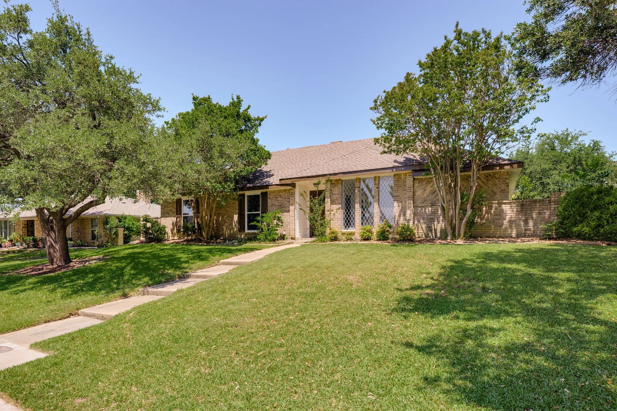 Brick facade residence featuring a front lawn with mature trees and a concrete pathway