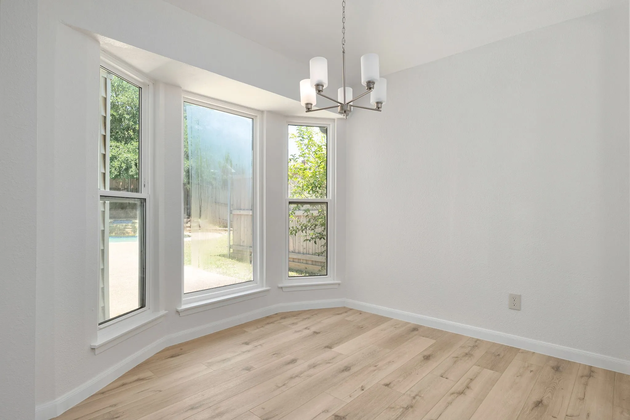 Bay window with white trim, wood-finish flooring, white walls, and a contemporary chandelier