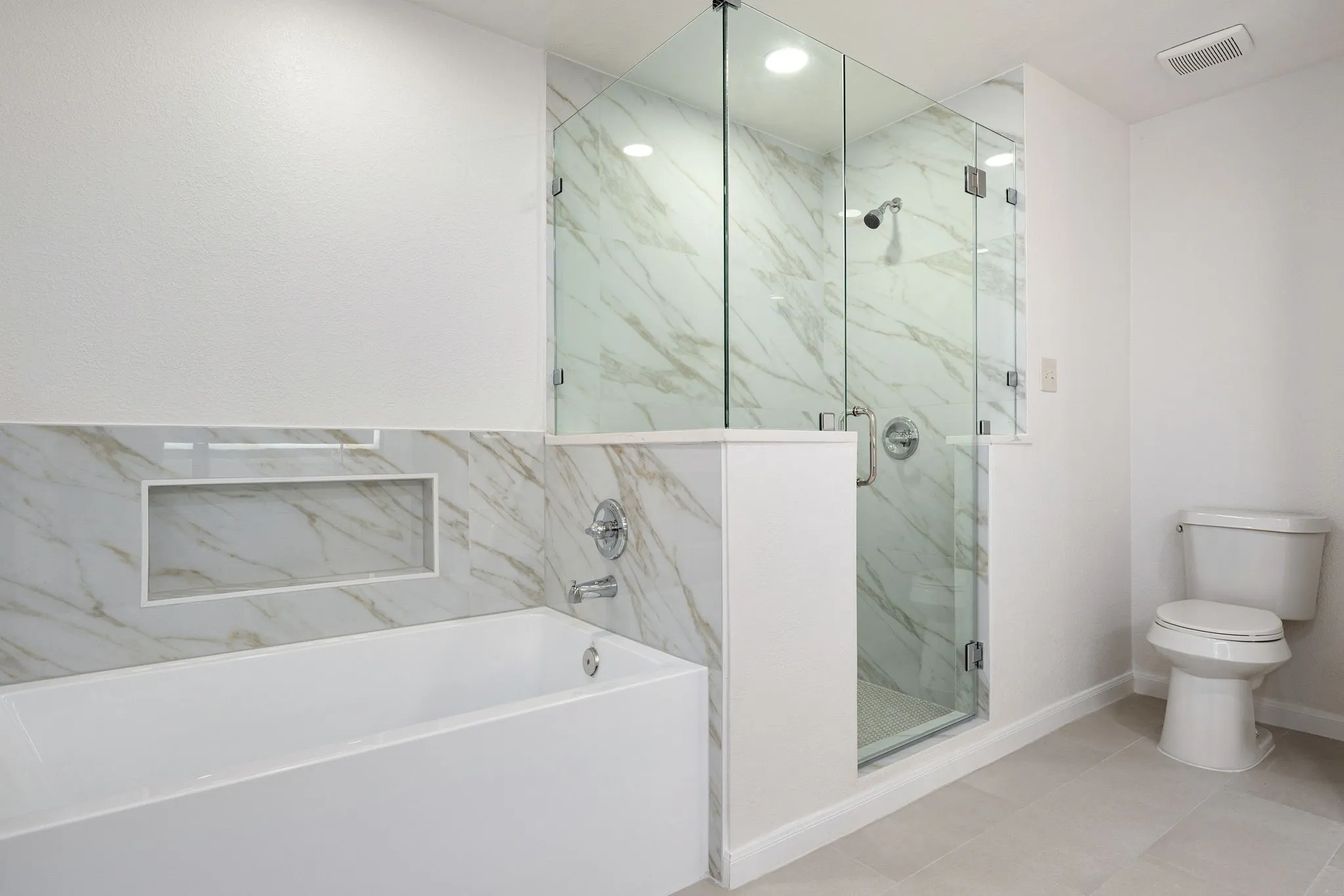 Contemporary bathroom featuring a freestanding tub, glass-enclosed shower, white marble-look wall tiling, recessed shower lighting, and light-toned floor tiling