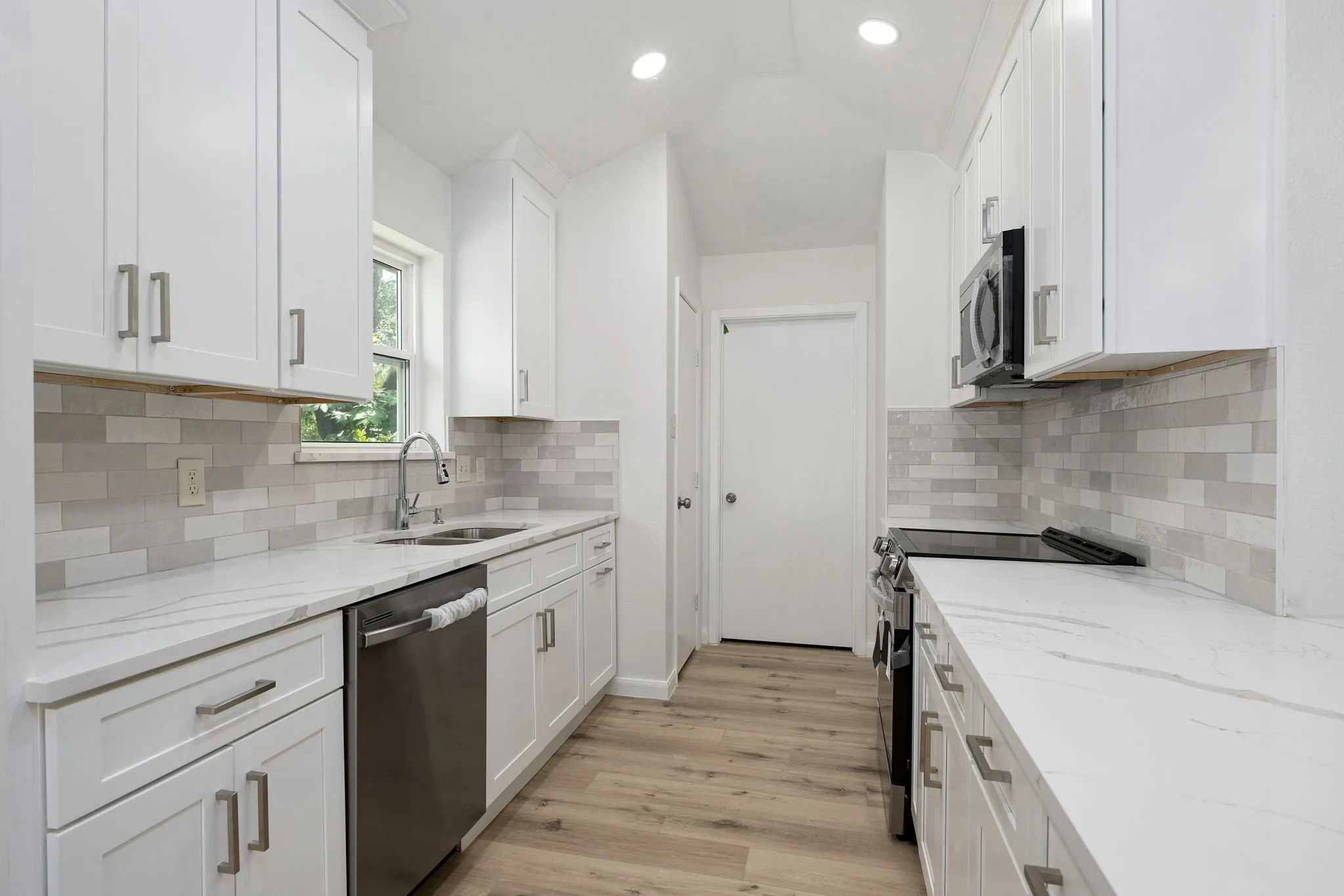 Modern kitchen featuring white shaker cabinetry, quartz countertops, a subway tile backsplash, stainless steel appliances, and wood-finish flooring
