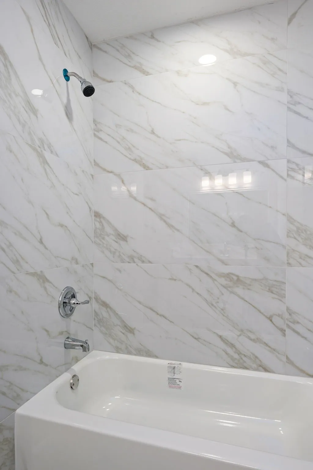 Shower and tub combination featuring white marble-patterned wall tiling and chrome fixtures