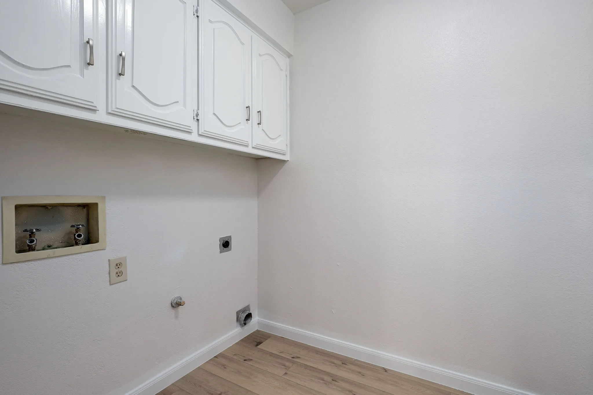 Laundry area featuring white cabinetry, light wood-finish flooring, and white baseboards