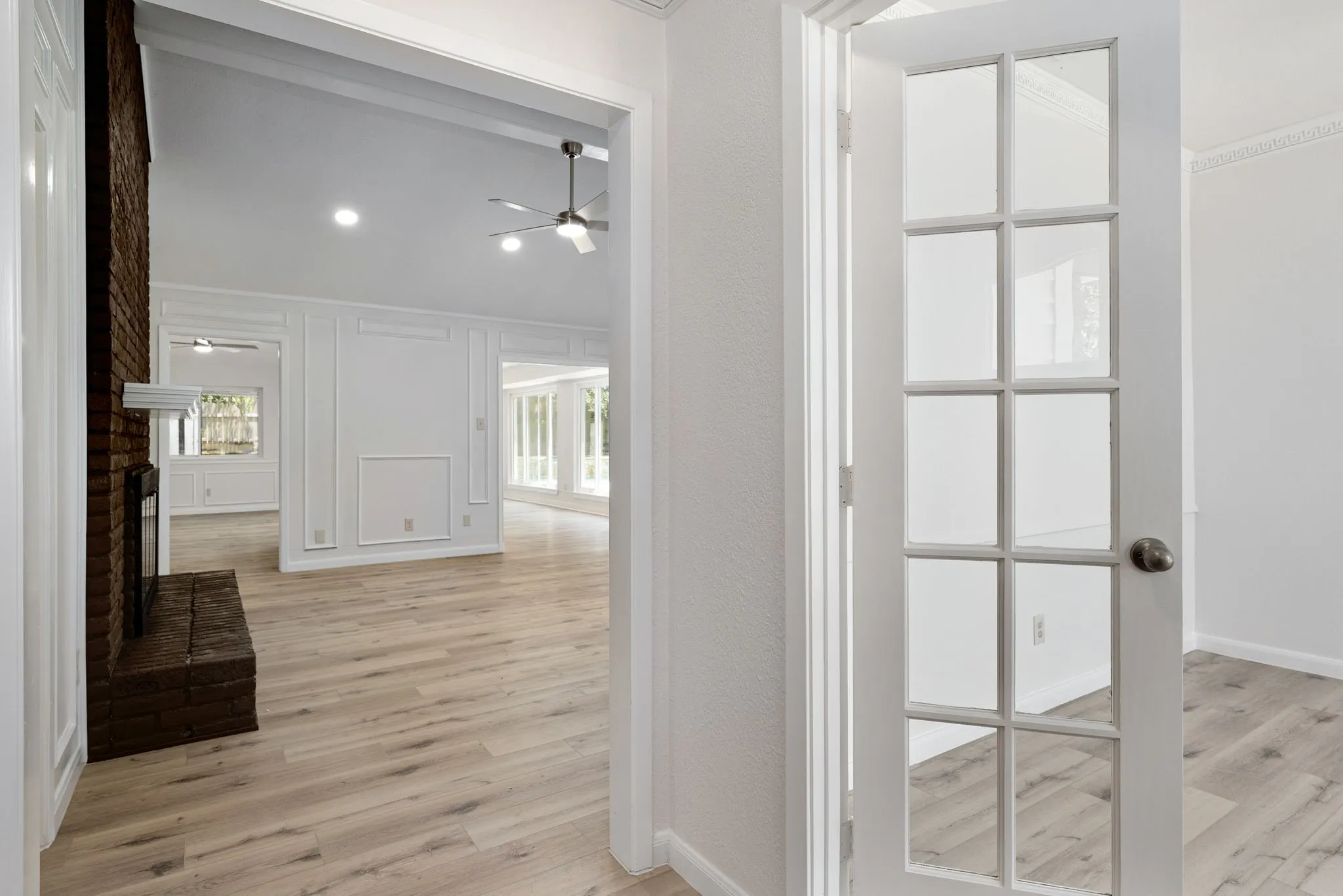 French doors open to an expansive living area featuring wood-finish flooring, a brick fireplace, a vaulted ceiling, recessed lighting, and decorative wall paneling