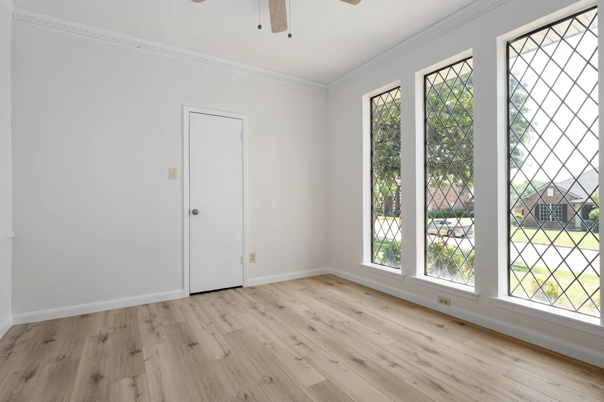 Room featuring three tall windows with diamond-patterned grilles, wood-finish flooring, a white door, and crown molding