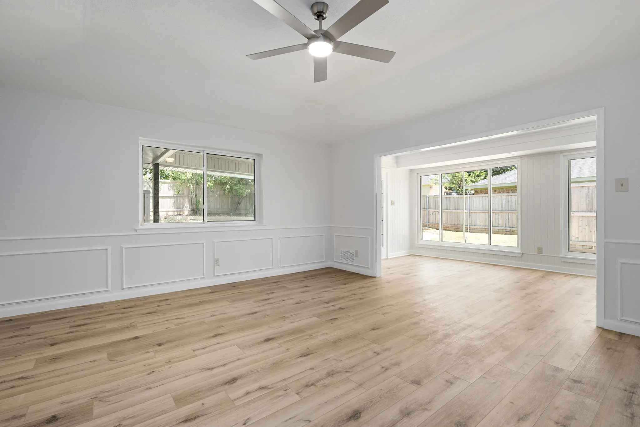 Open living area featuring light wood-finish flooring, white paneling, and a modern ceiling fan