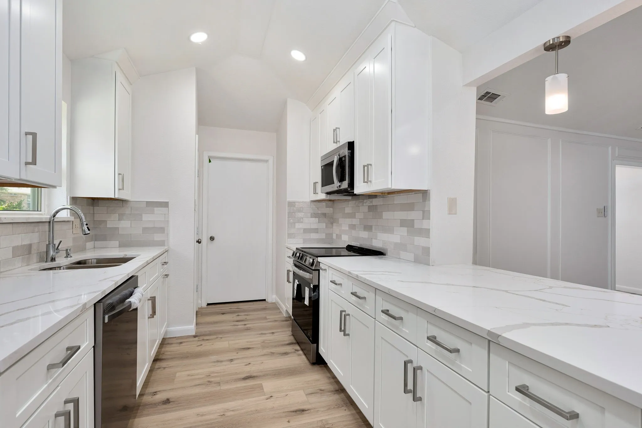 Contemporary kitchen with white shaker cabinetry, light-toned wood-finish flooring, and a subway tile backsplash