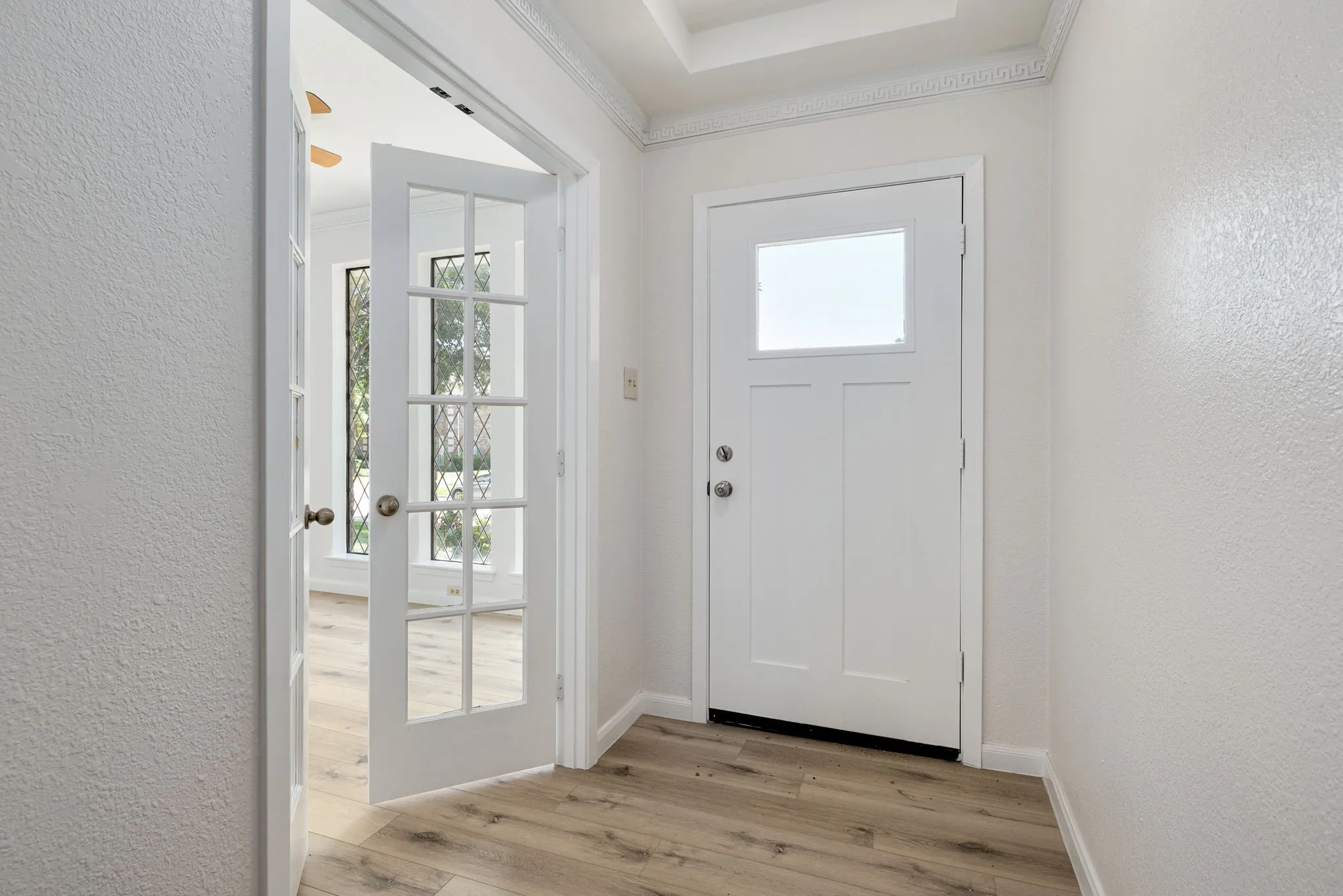 Entryway featuring light wood-finish flooring, a white front door with a square window, and decorative crown molding