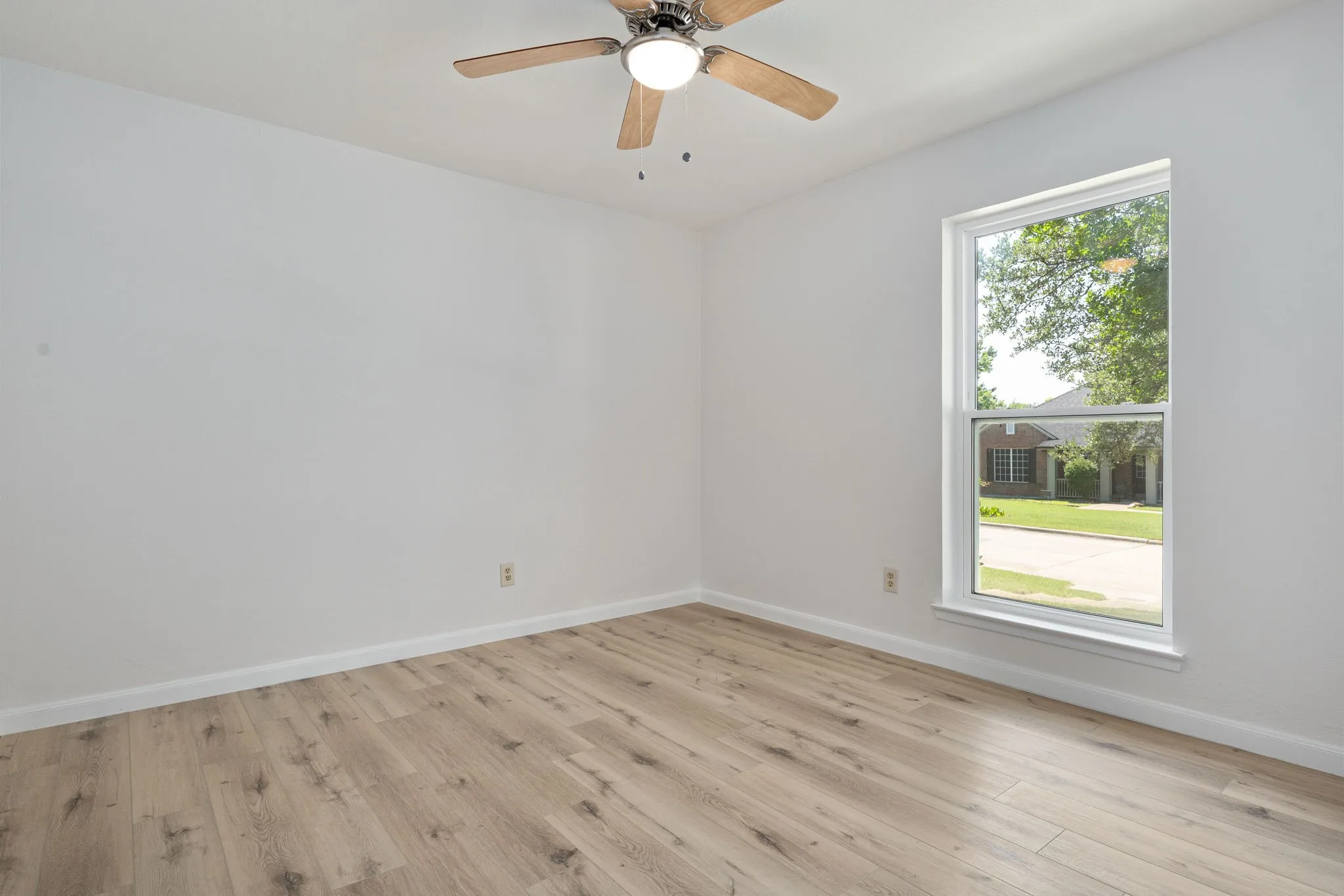 Spacious room featuring wood-finish flooring, crisp white walls, and a large window
