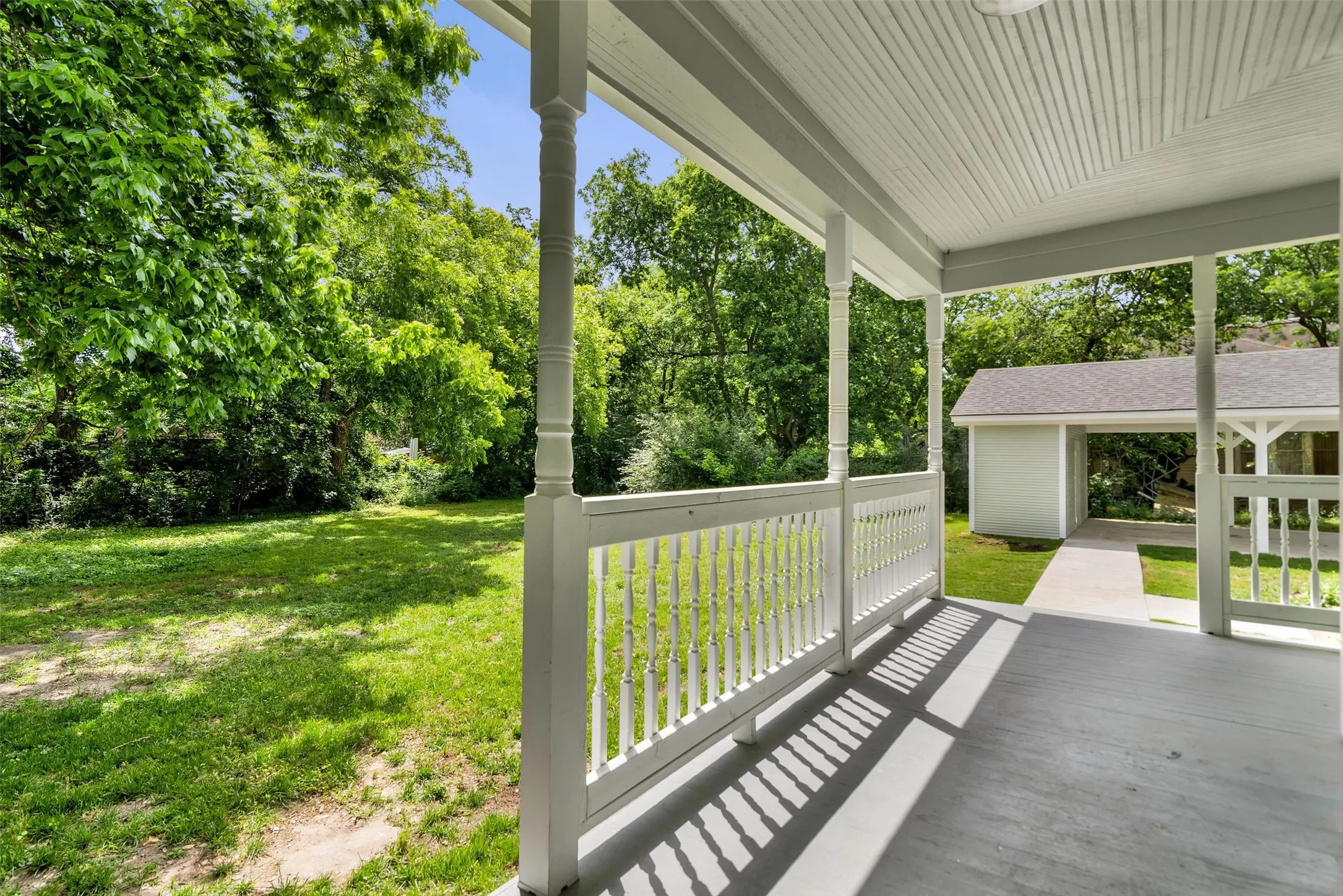 Spacious covered porch with white painted balusters and posts, featuring a paneled ceiling and painted flooring