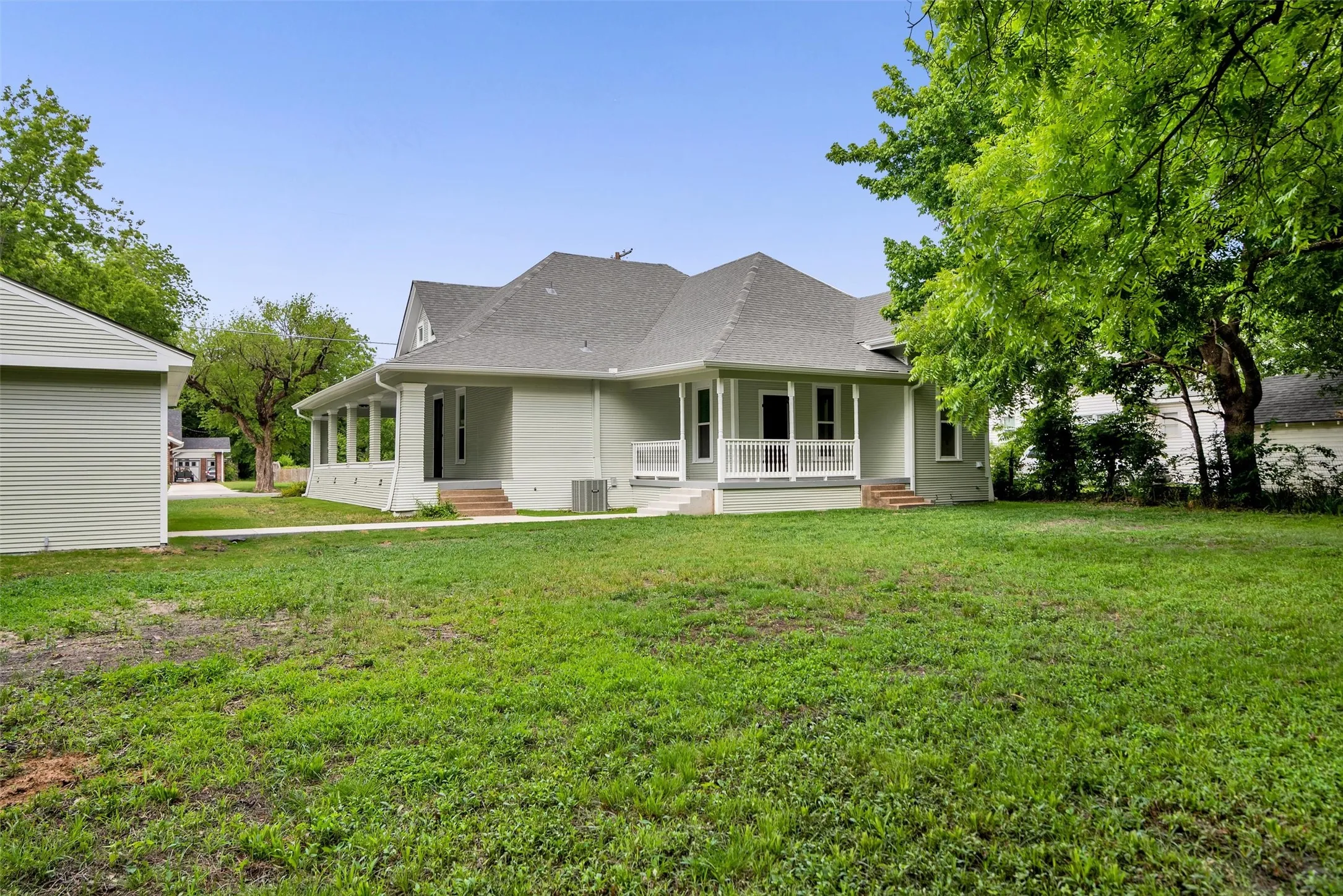 Spacious exterior featuring light green siding, a dark gray shingled roof, a covered porch with white railings, and a detached structure