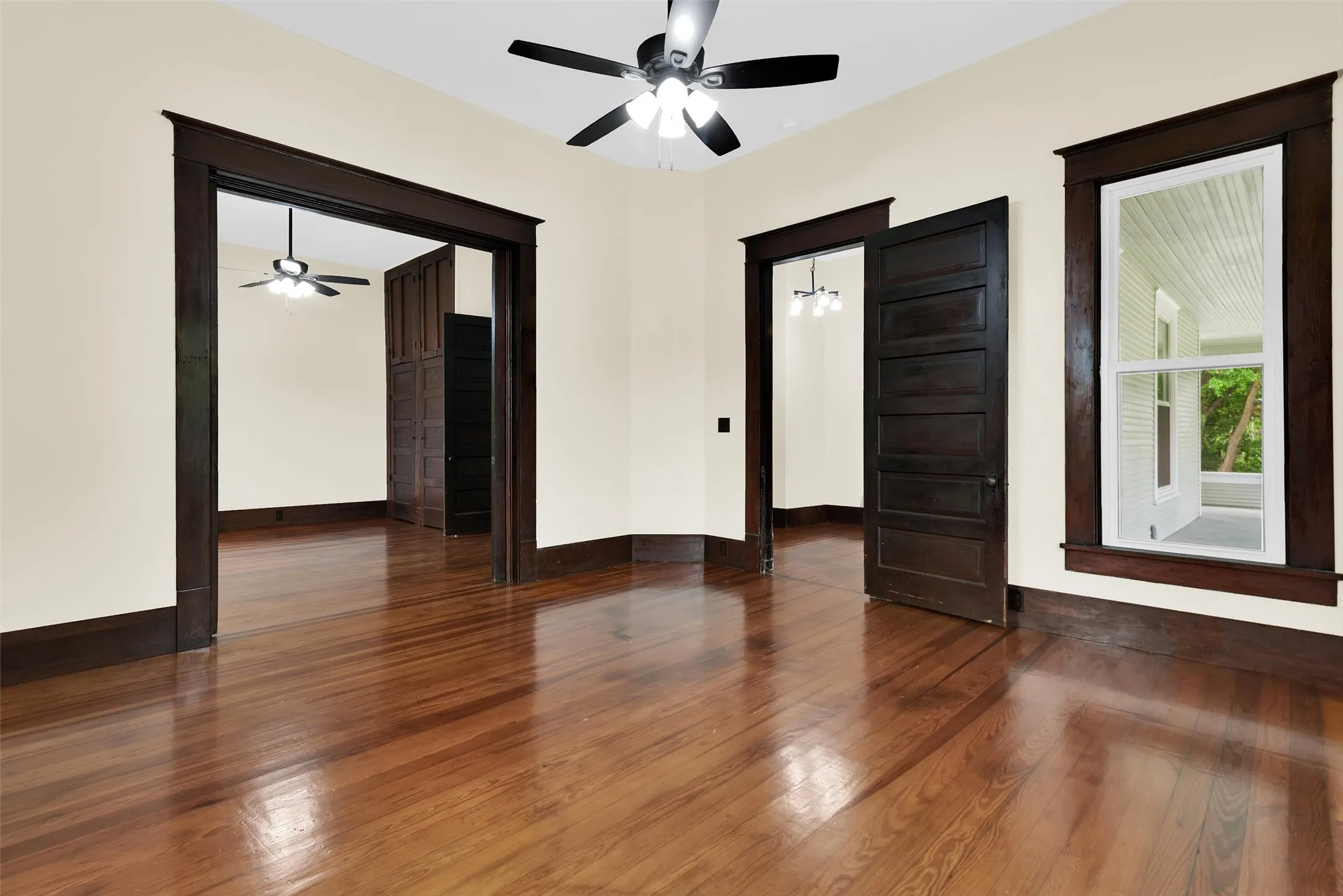 Spacious room featuring rich wood-finish flooring, dark wood trim, classic five-panel doors, and an overhead ceiling fan