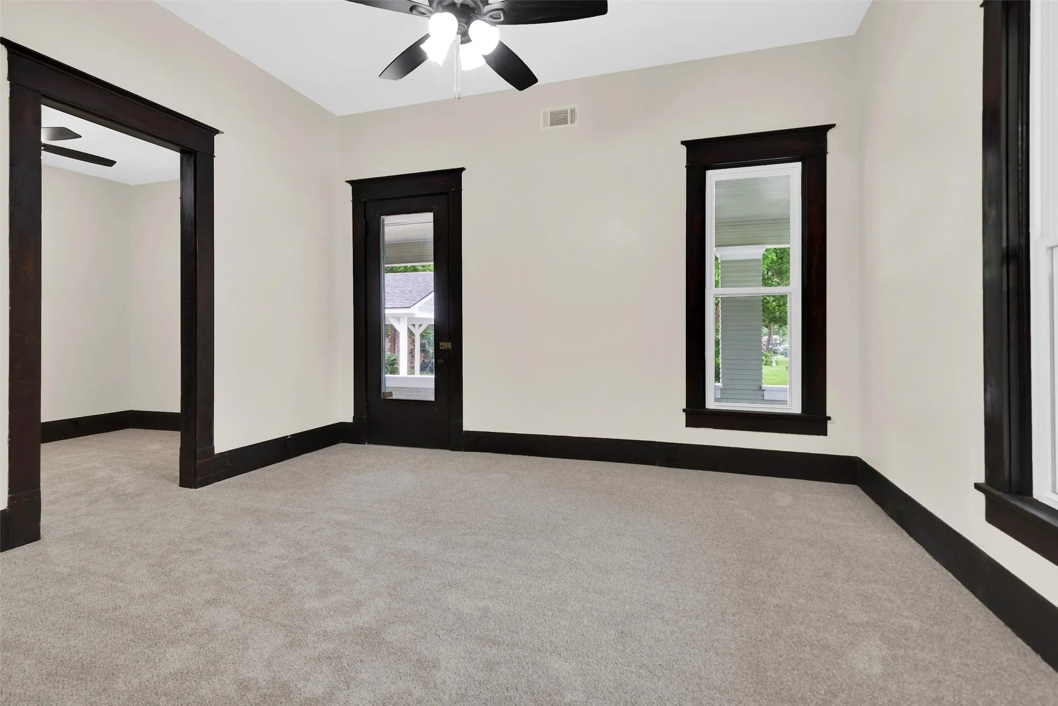 Bright interior space featuring rich wood flooring, contrasting dark wood trim, light neutral wall color, and a ceiling fan