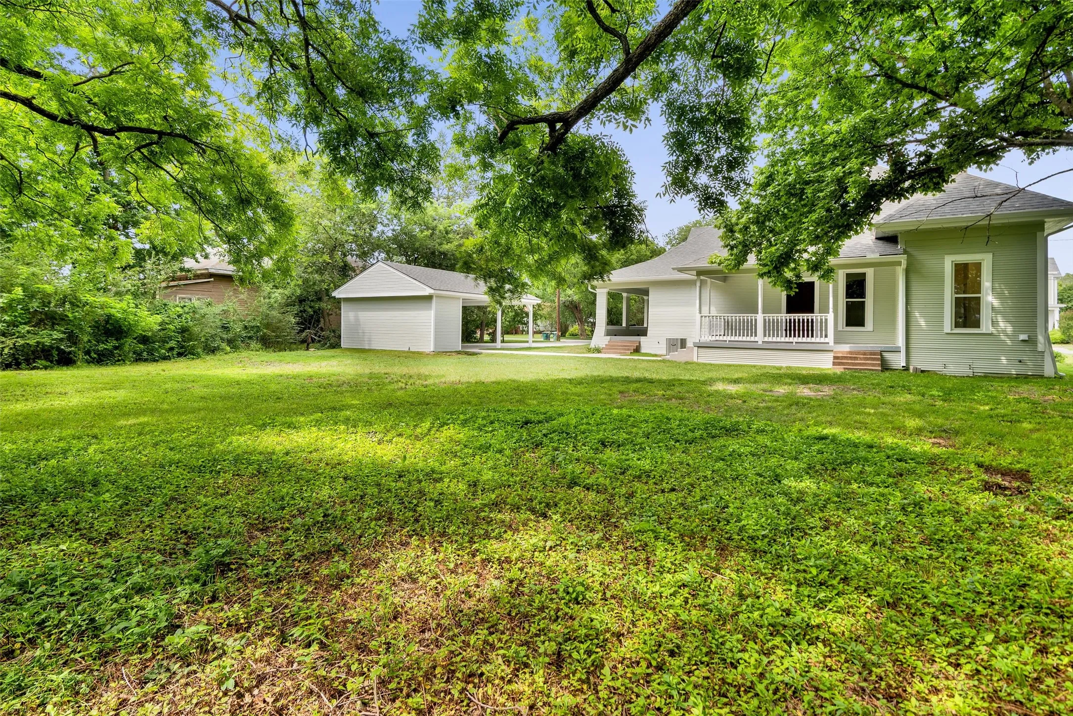 Expansive lawn area featuring mature trees and a detached garage with an attached carport