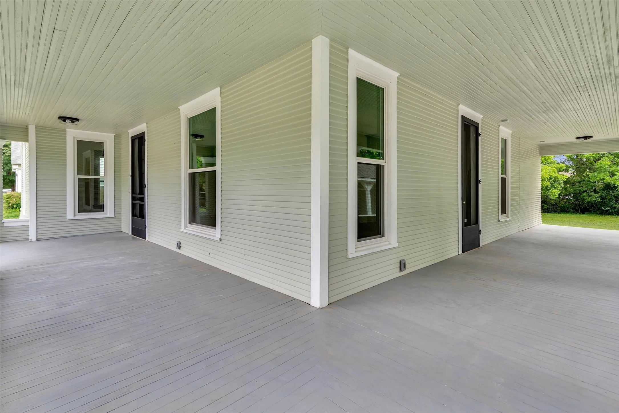 Expansive covered porch featuring light gray horizontal siding, white trim, and a matching light gray painted floor