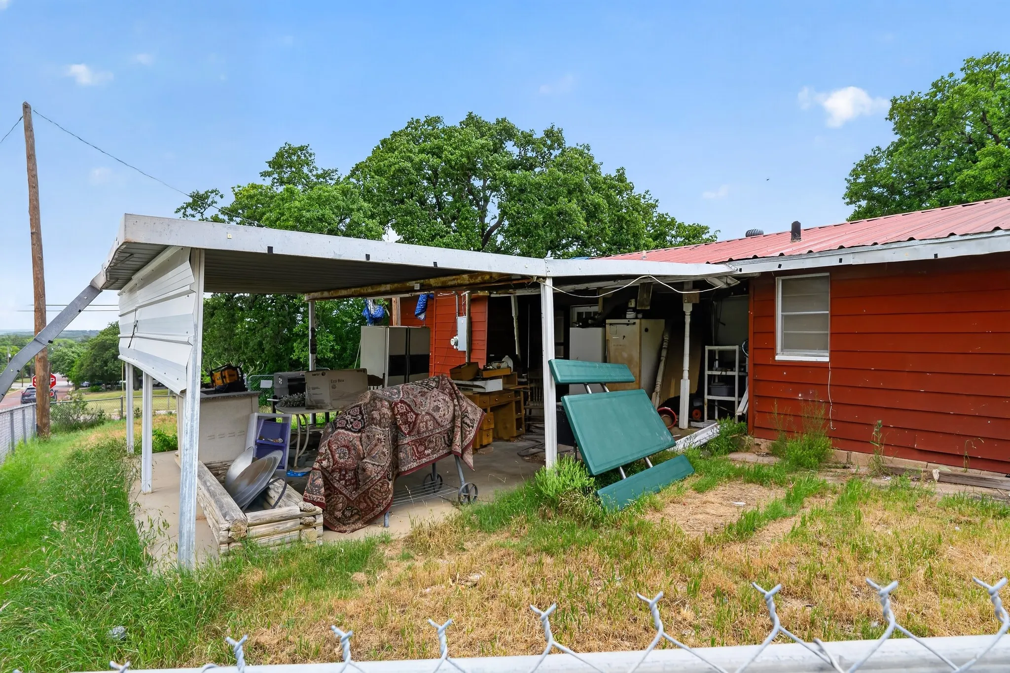 Rear exterior view of the structure highlighting a large metal-awning covered back patio slab, vertical red wood siding panels, and an open grass lot line.