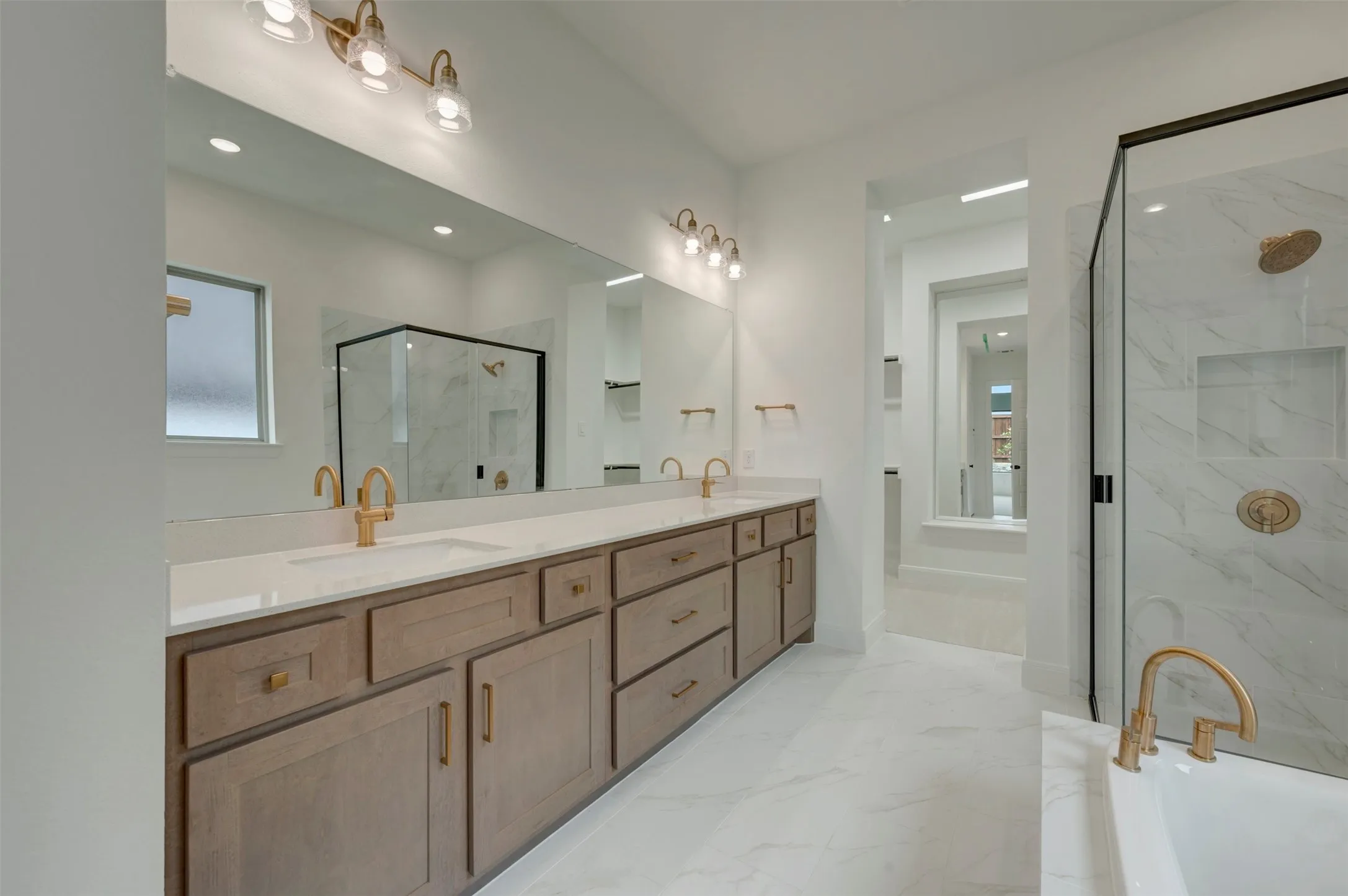 Spa-inspired primary bathroom featuring a wood-finish double vanity with brass hardware, white quartz countertops, and dual vessel sinks beneath a frameless mirror