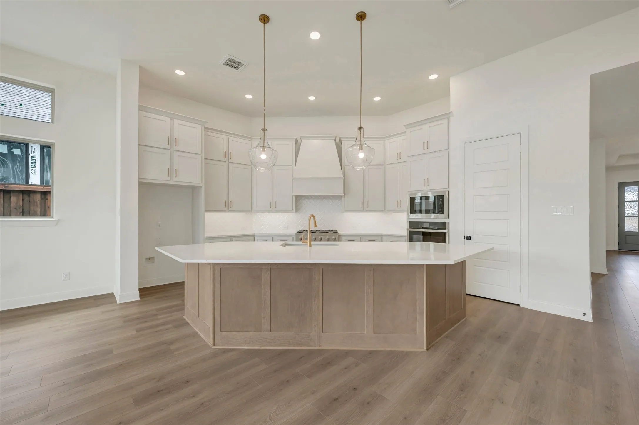 Gourmet kitchen with an expansive island, white shaker cabinetry, stainless steel appliances, and wood-finish flooring