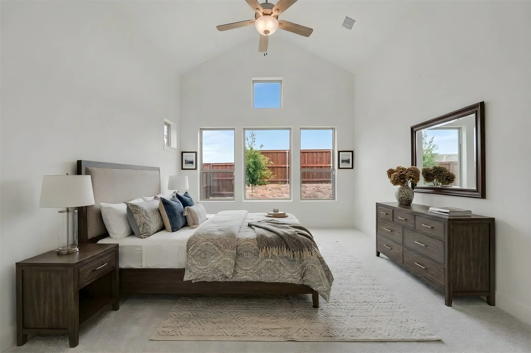 Vaulted ceiling with a ceiling fan, multiple windows providing ample natural light, and light-toned carpeting