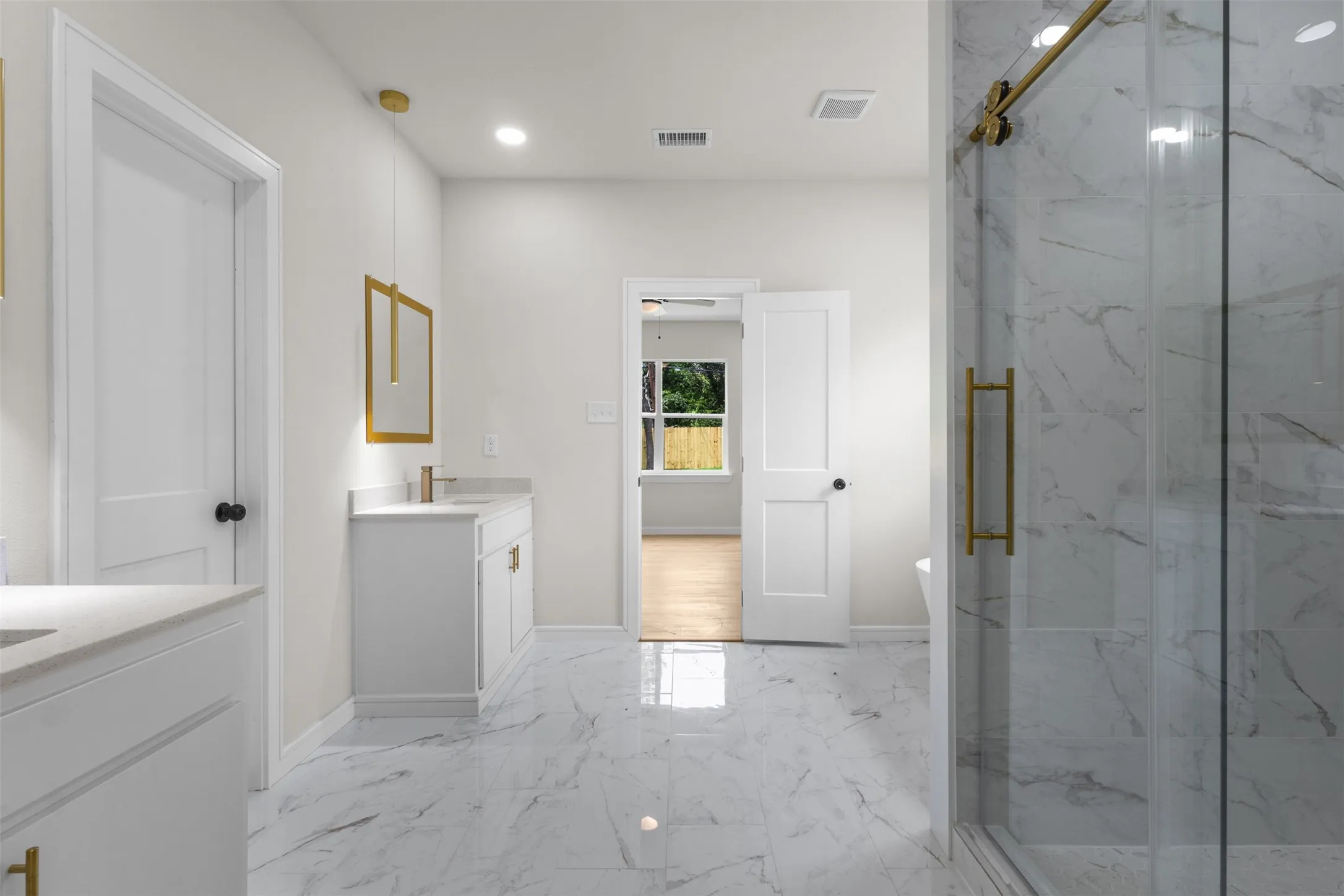 Spacious bathroom featuring marble-look tile flooring, a glass-enclosed shower with gold-tone hardware, and dual white vanity cabinets with integrated sinks and gold-tone fixtures