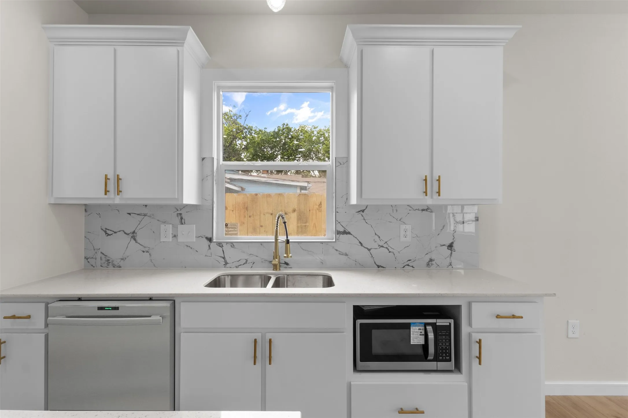 Kitchen featuring white cabinetry with gold-finish hardware, a white countertop, and a marble-patterned backsplash