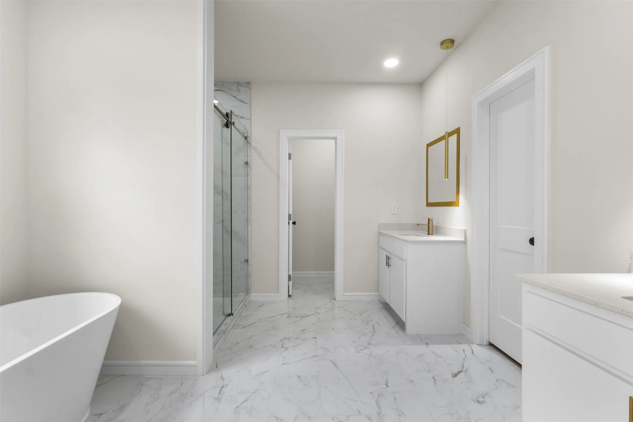 Spacious bathroom featuring a freestanding soaking tub, a walk-in shower with a glass enclosure and tiled surround, dual vanity areas with white cabinetry and light countertops, and large format marble-look floor tiling