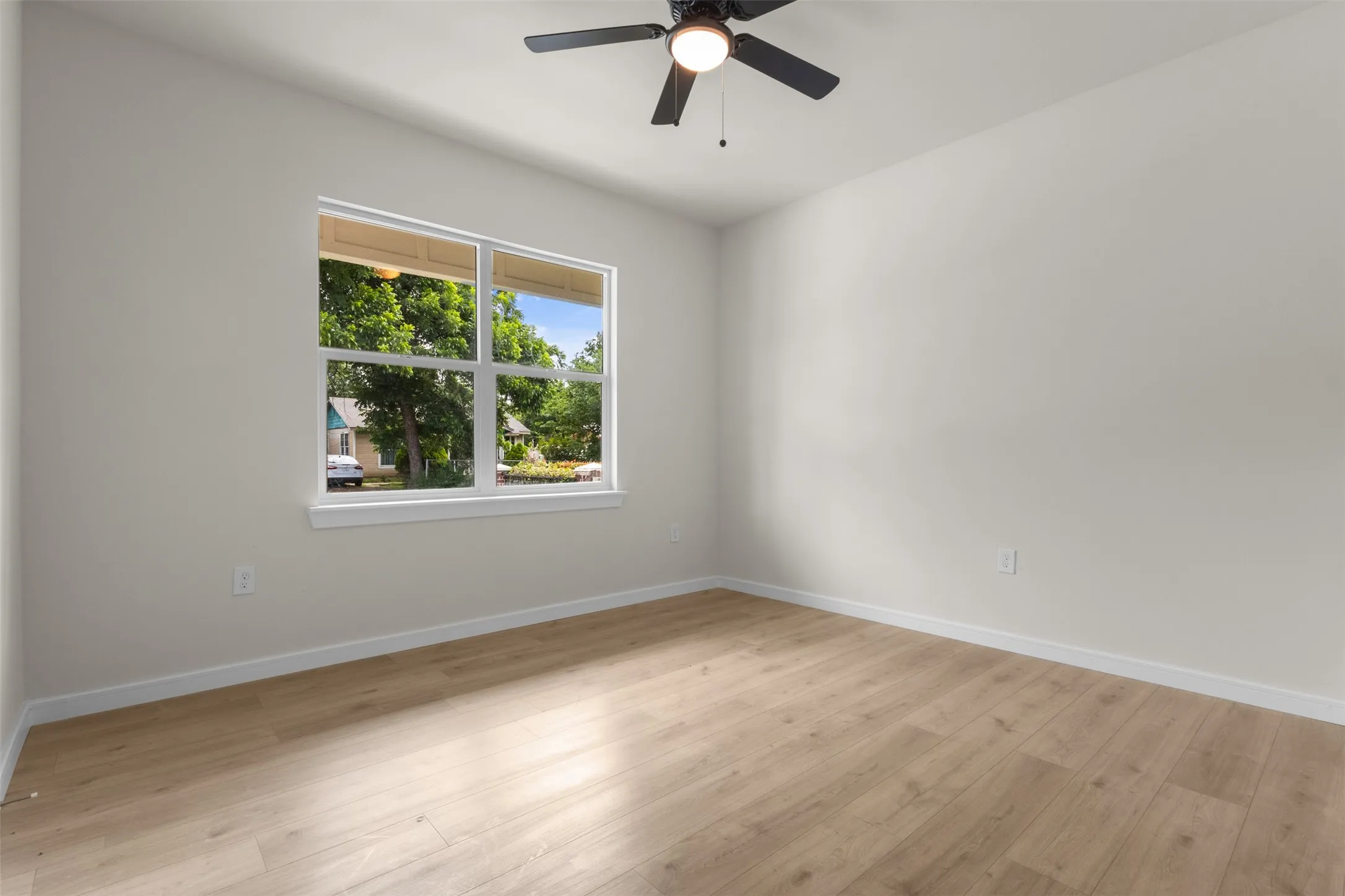 Spacious room featuring light wood-finish flooring, a contemporary ceiling fan, and a large window with white trim