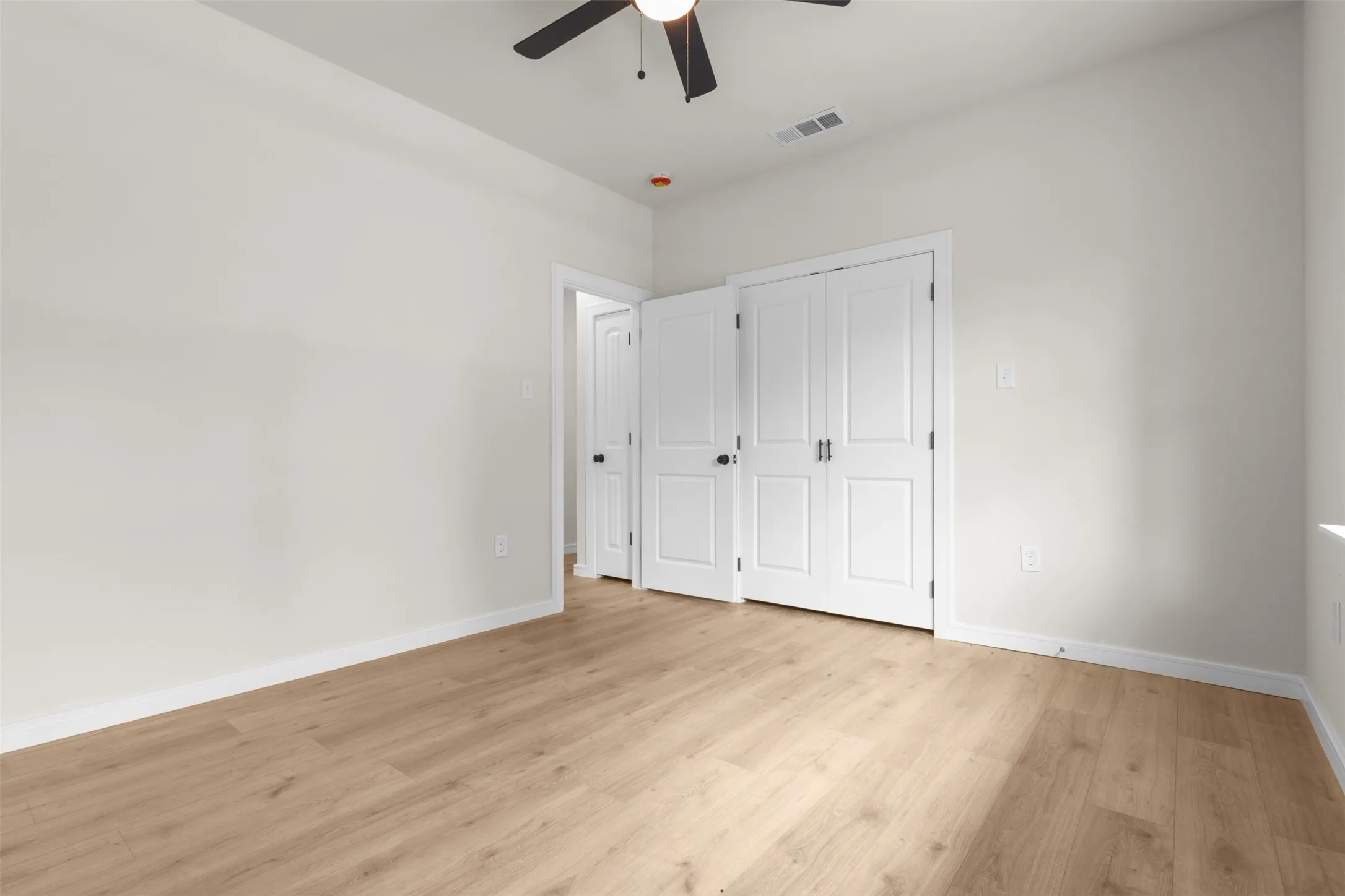 Spacious interior room featuring wood-finish flooring, white walls, and a ceiling fan