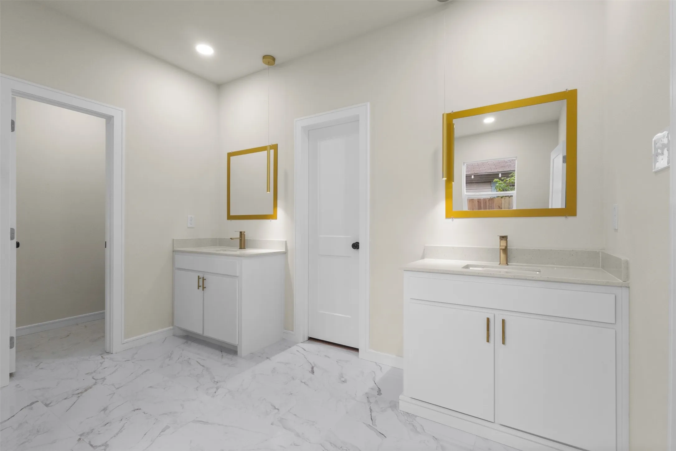 Bathroom featuring dual white vanities with light countertops, gold-framed mirrors, and brass-finish fixtures