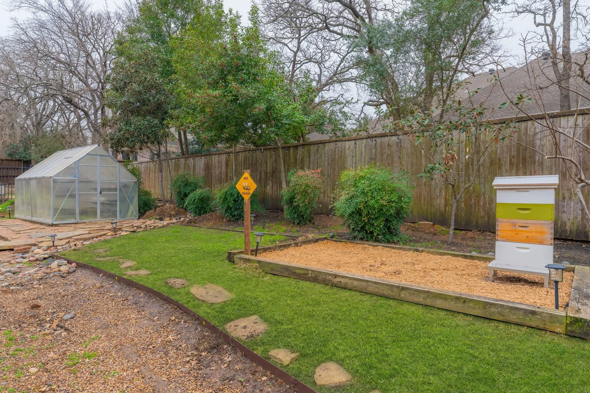 Backyard featuring a clear-paneled greenhouse, a raised garden bed with wood chip fill, and a painted beehive