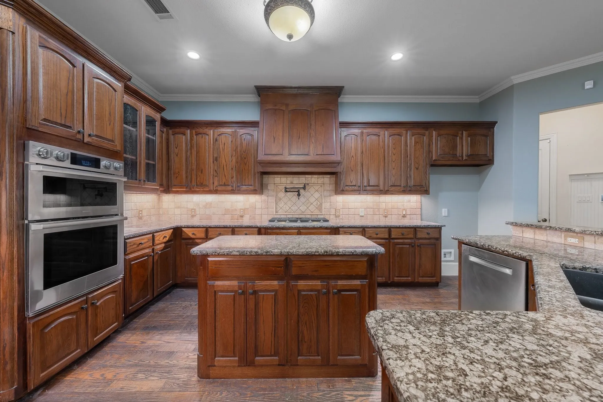 Kitchen featuring wood-finish cabinetry, granite countertops, stainless steel double ovens, a built-in dishwasher, and an island with additional storage