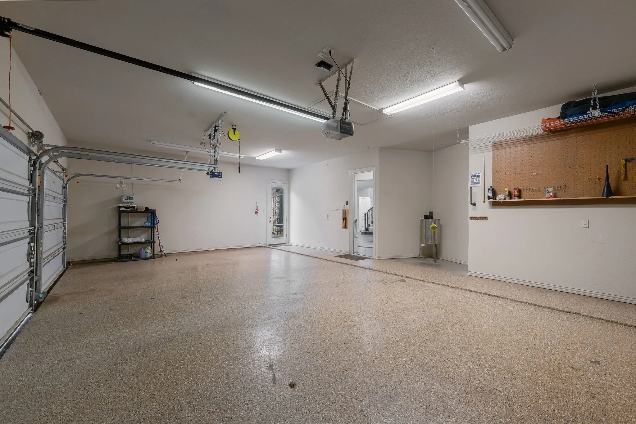Spacious two-car garage featuring an epoxy-coated concrete floor, bright overhead fluorescent lighting, and an integrated workbench with shelving