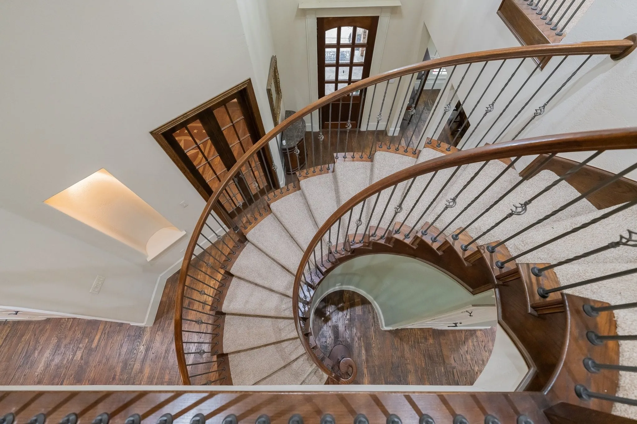 Grand spiral staircase featuring wood-finish treads and handrails, wrought iron balusters, and a carpet runner
