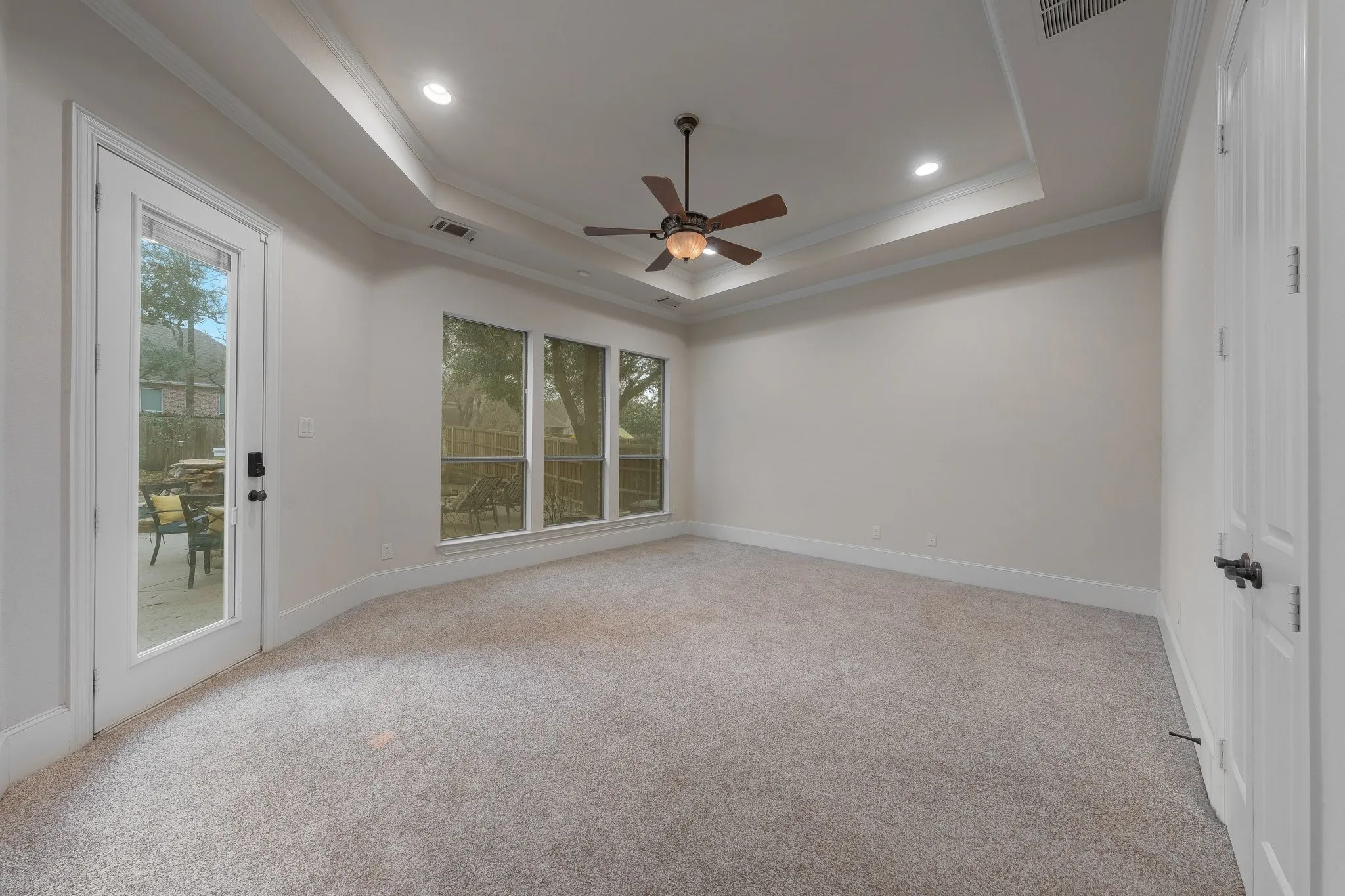 Spacious room featuring light-colored carpeting, a tray ceiling with recessed lighting, and a ceiling fan
