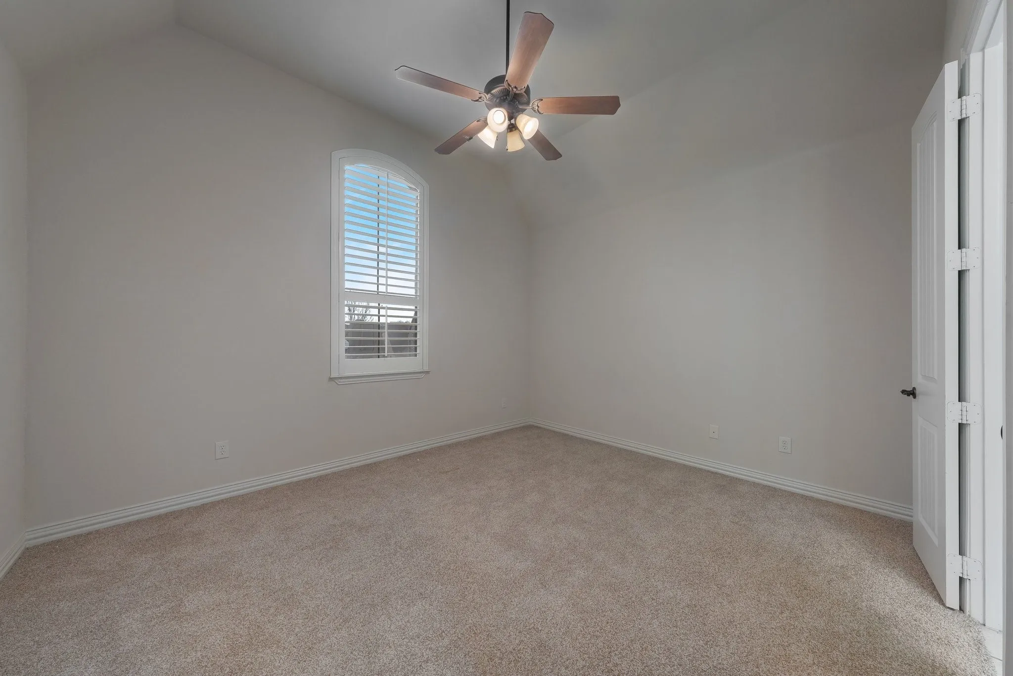 Carpeted room featuring a vaulted ceiling and an arched window with white plantation shutters