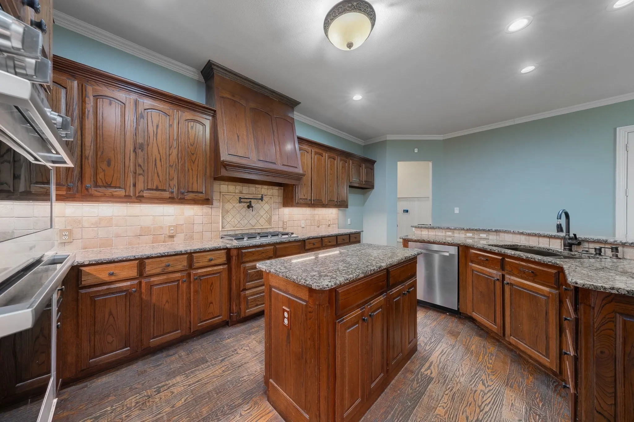 Kitchen featuring a central island, wood-finish flooring, granite countertops, stainless steel appliances, and a tiled backsplash