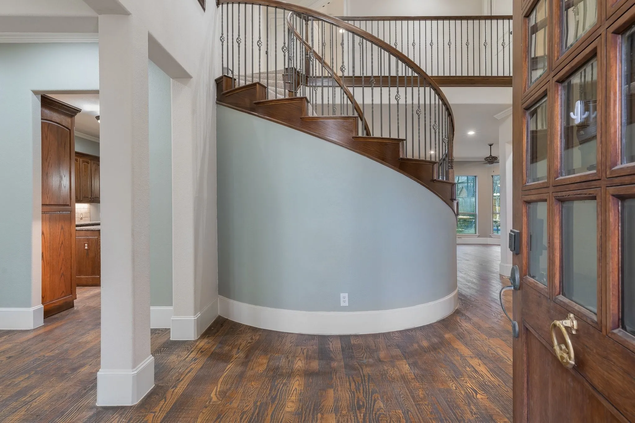 Grand entry hall featuring a curved wood staircase with ornate iron balusters, rich wood-finish flooring, and a multi-paneled front door