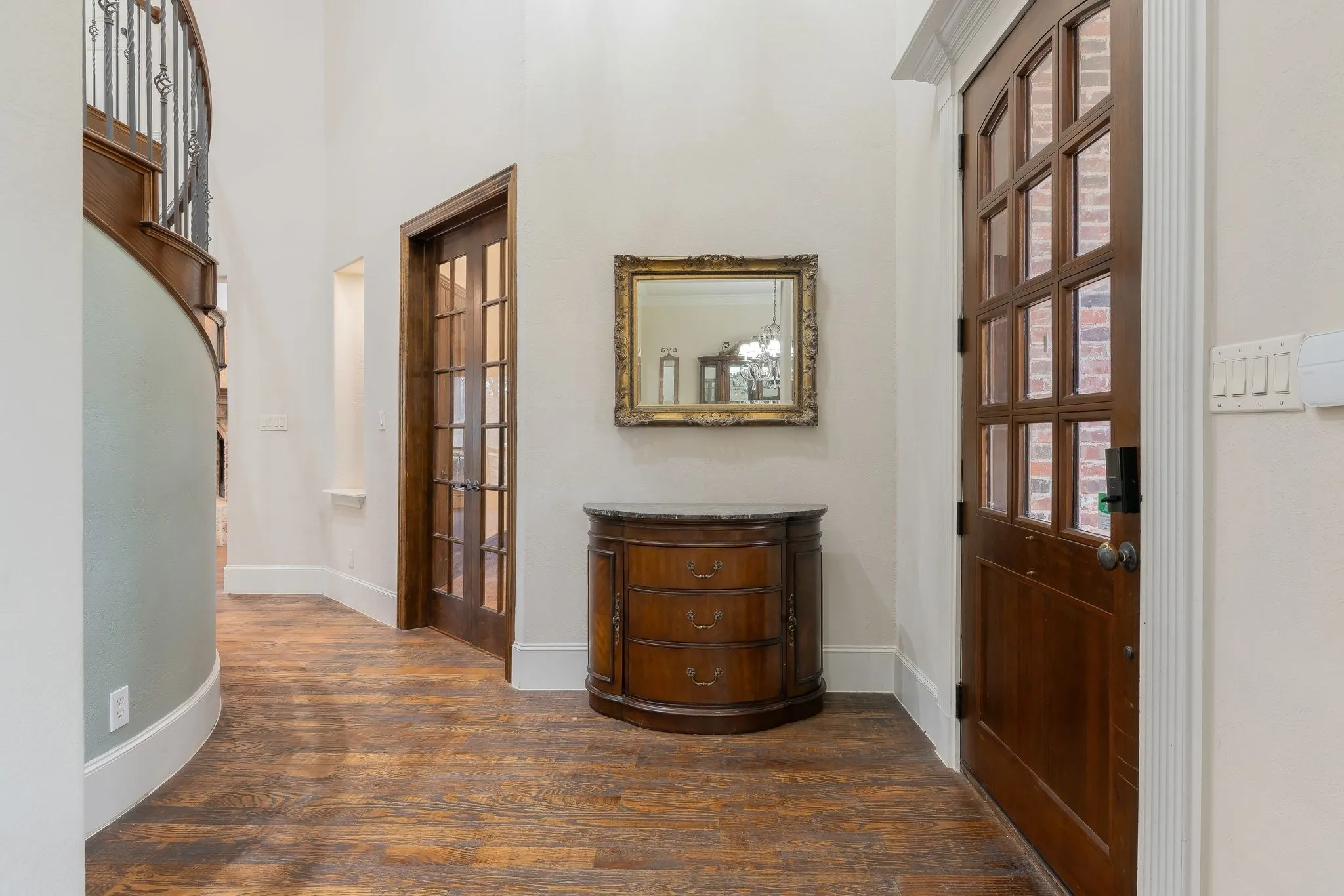 Entryway featuring wood-finish flooring, a curved staircase with wrought iron balusters, a dark wood front door with glass panels, and a glass-paned interior door