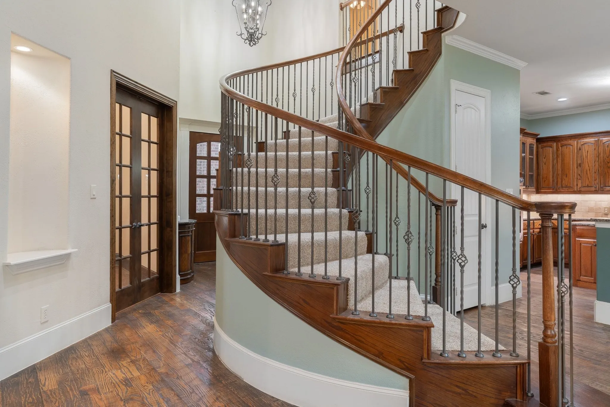 Grand curved staircase featuring wood treads and risers, carpeted steps, and decorative wrought iron balusters