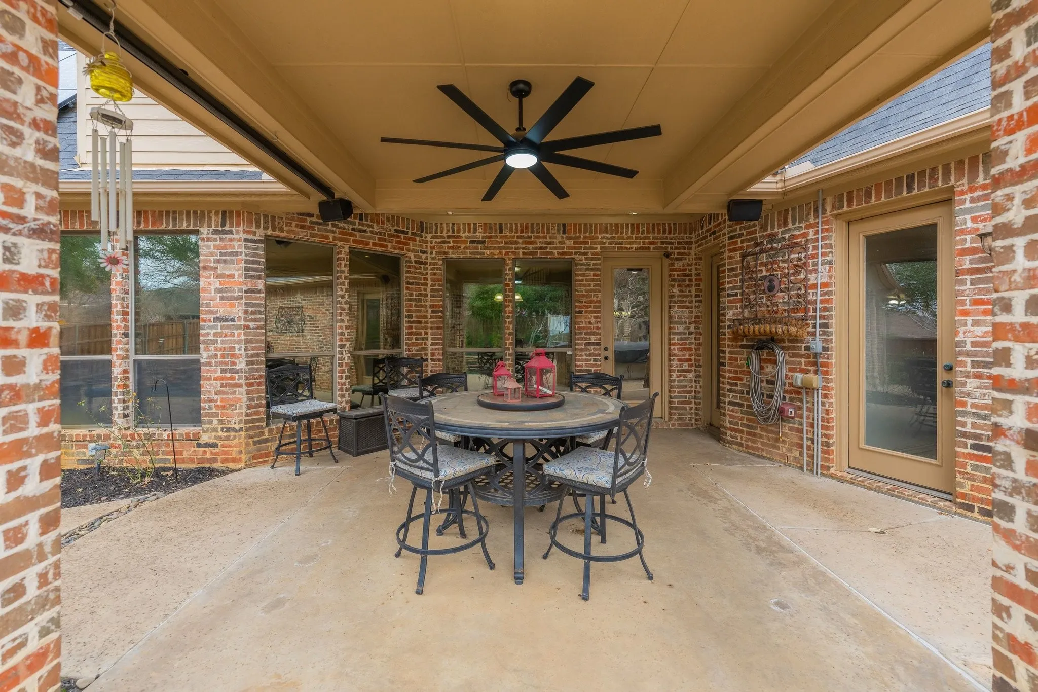Covered patio featuring a ceiling fan with integrated lighting, brick exterior walls, and multiple glass-paned doors