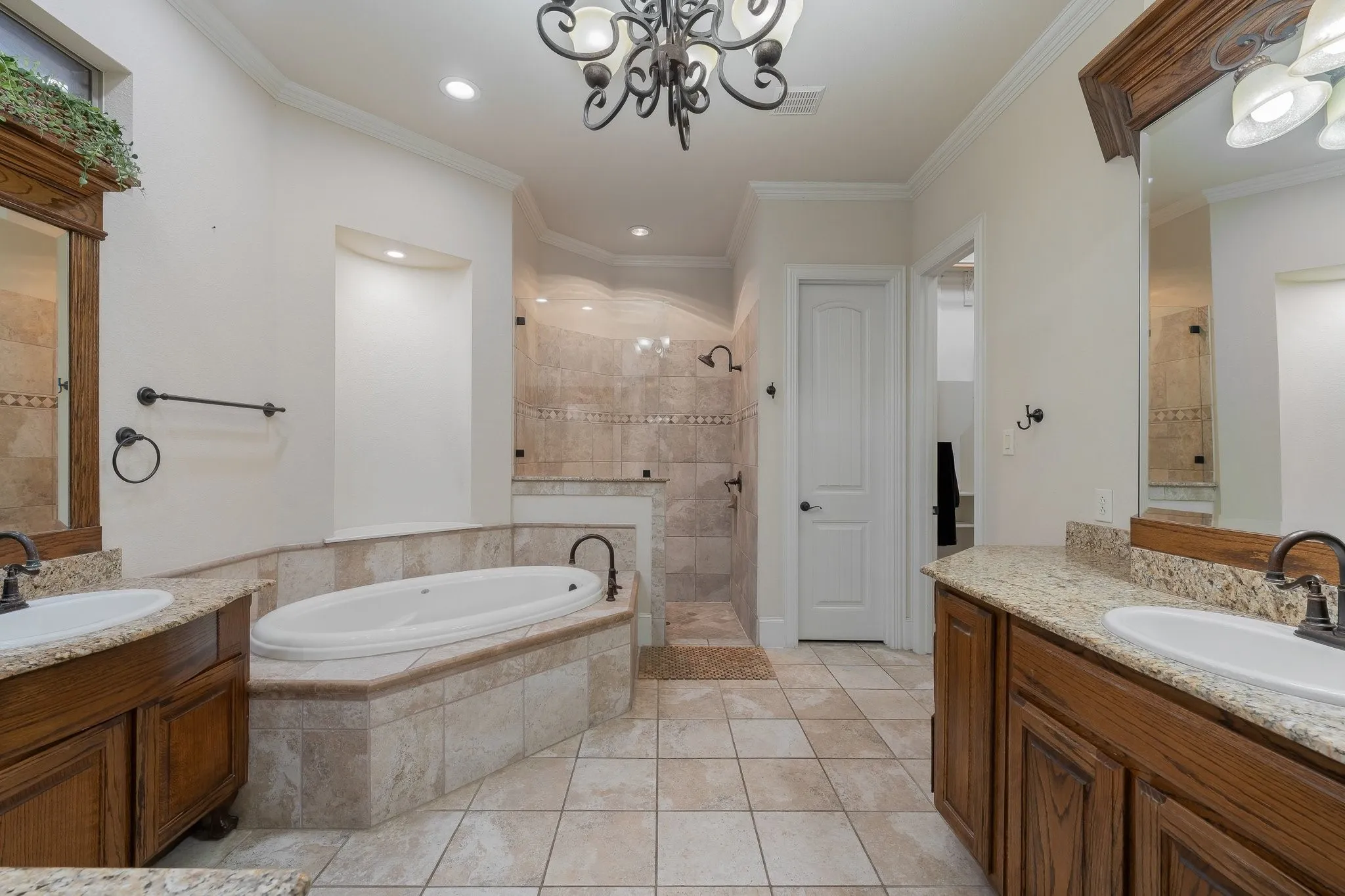 Spa-inspired bathroom featuring a built-in soaking tub, a spacious walk-in shower with tile surround, dual vanity sinks with granite countertops, rich wood-finish cabinetry, and ceramic tile flooring