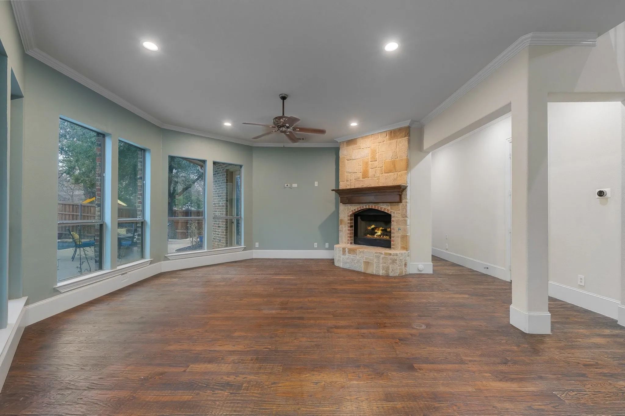 Spacious living area featuring wood-finish flooring, a stone-clad corner fireplace with a dark wood mantel, and multiple large windows
