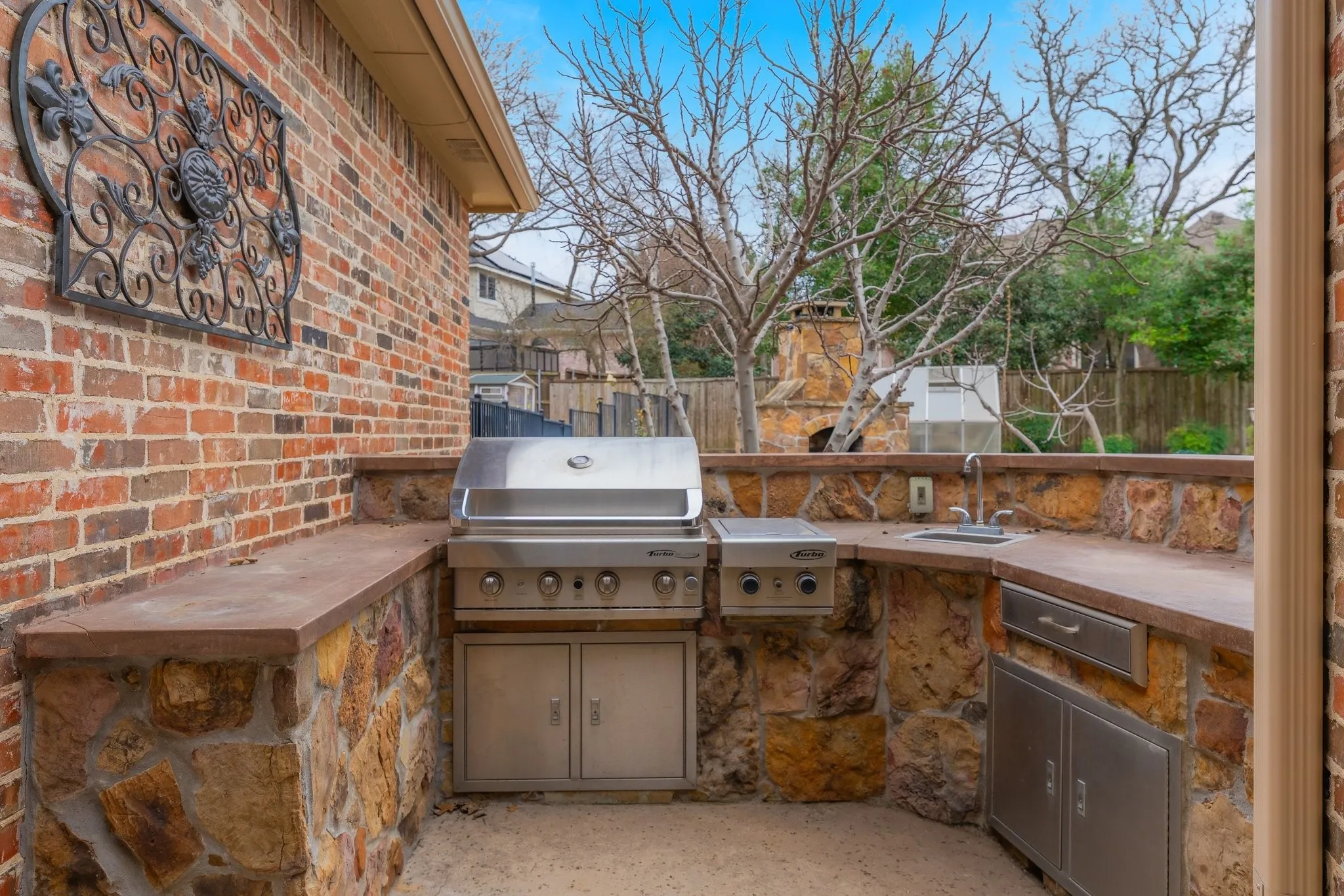 Outdoor kitchen featuring a built-in stainless steel grill, integrated sink, and stone-clad base with countertop space
