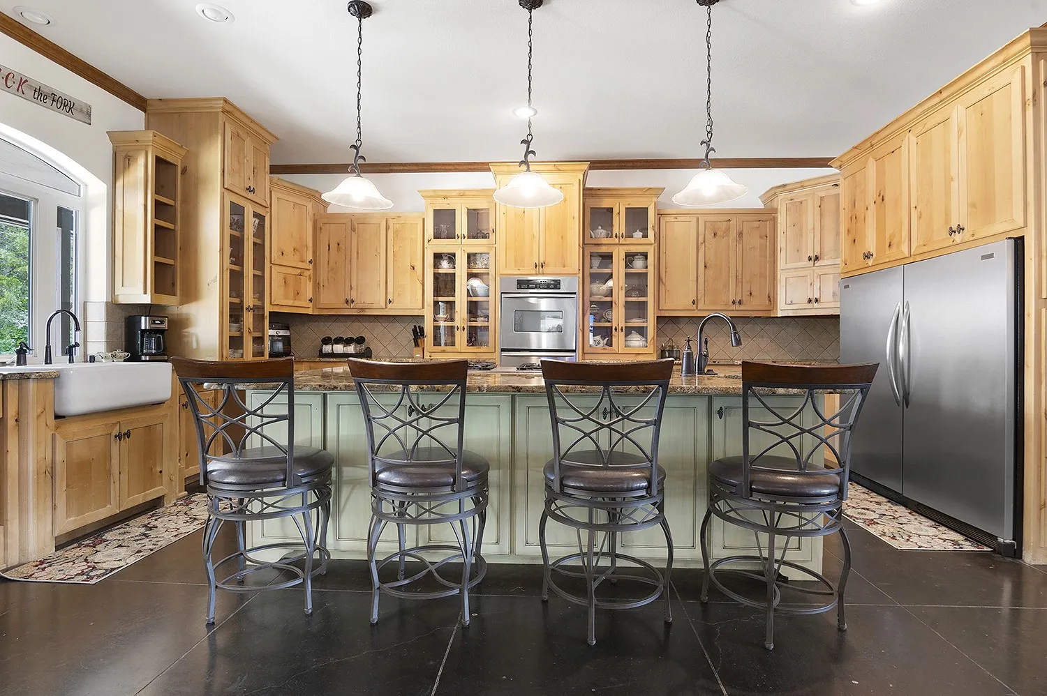 Kitchen featuring a spacious island with seating, natural wood cabinetry, integrated stainless steel appliances, a farmhouse sink, and pendant lighting