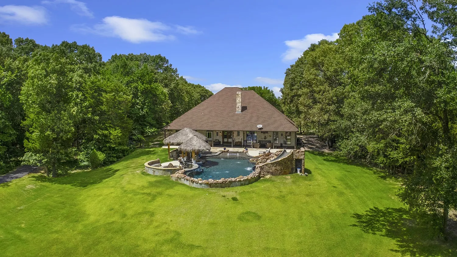 Expansive rear exterior featuring a multi-level pool with rock accents, an attached spa, and a thatched-roof tiki bar