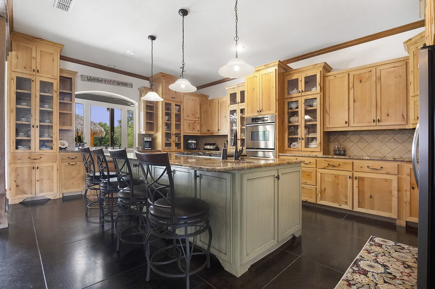 Spacious kitchen featuring extensive wood cabinetry, a large central island with seating, dark flooring, stainless steel appliances, and a tiled backsplash