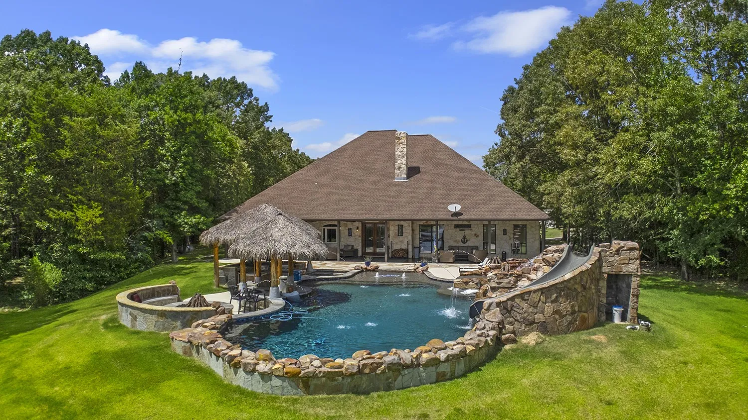 Expansive backyard featuring a large swimming pool with water features, a built-in slide, and hot tub