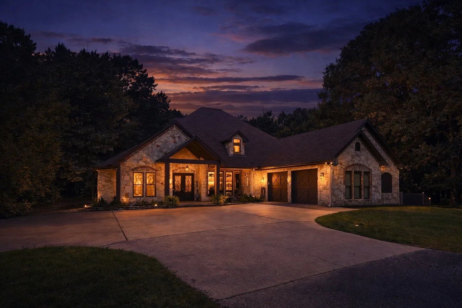 Stone exterior home featuring a concrete driveway, two dark garage doors, and illuminated entryway
