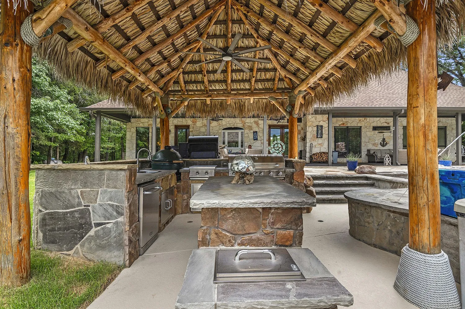 Outdoor kitchen featuring a thatched roof pavilion, stone countertops, integrated sink, and built-in grill