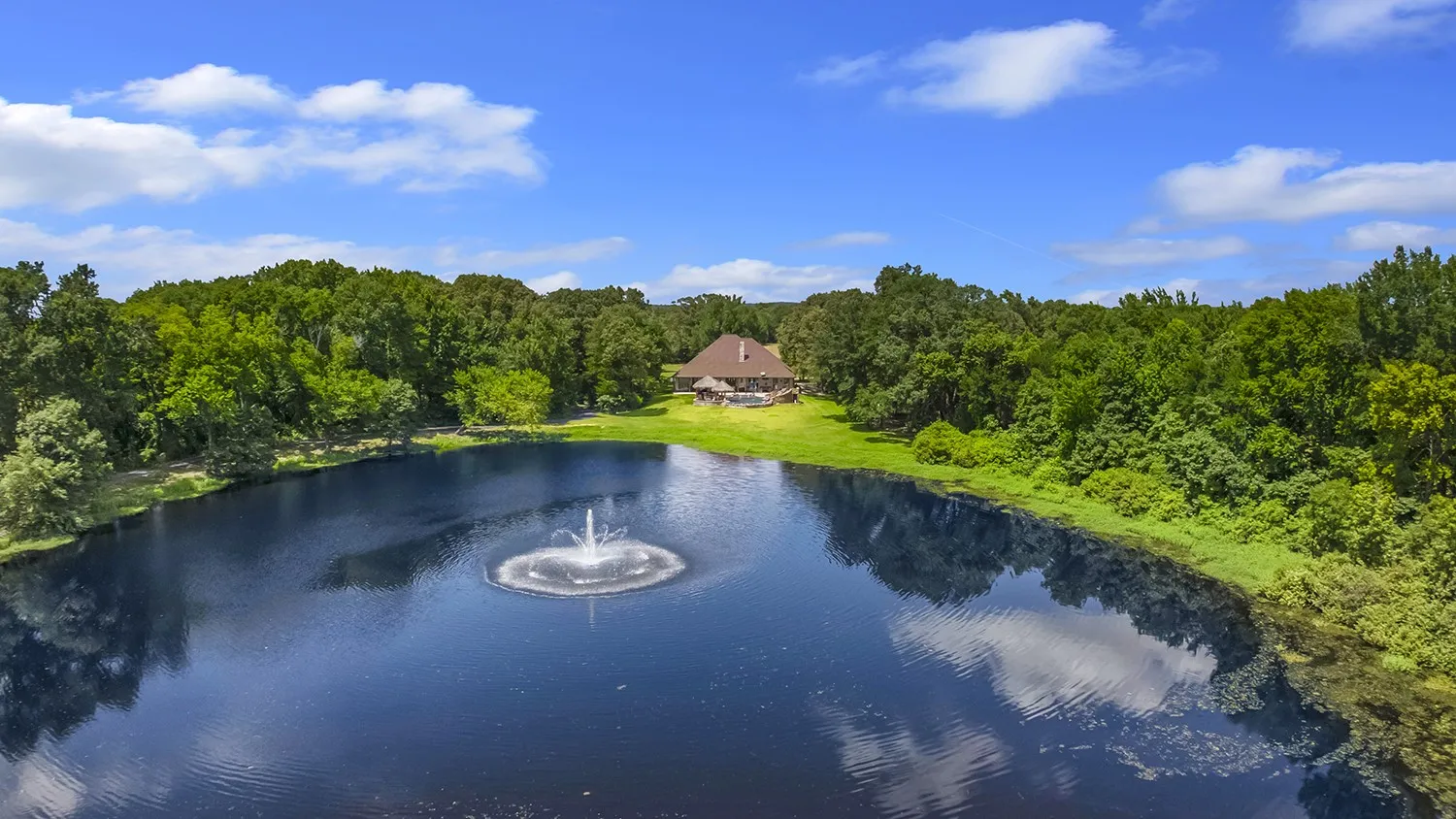 Expansive private lake with a central fountain feature, surrounded by mature trees and lush landscaping