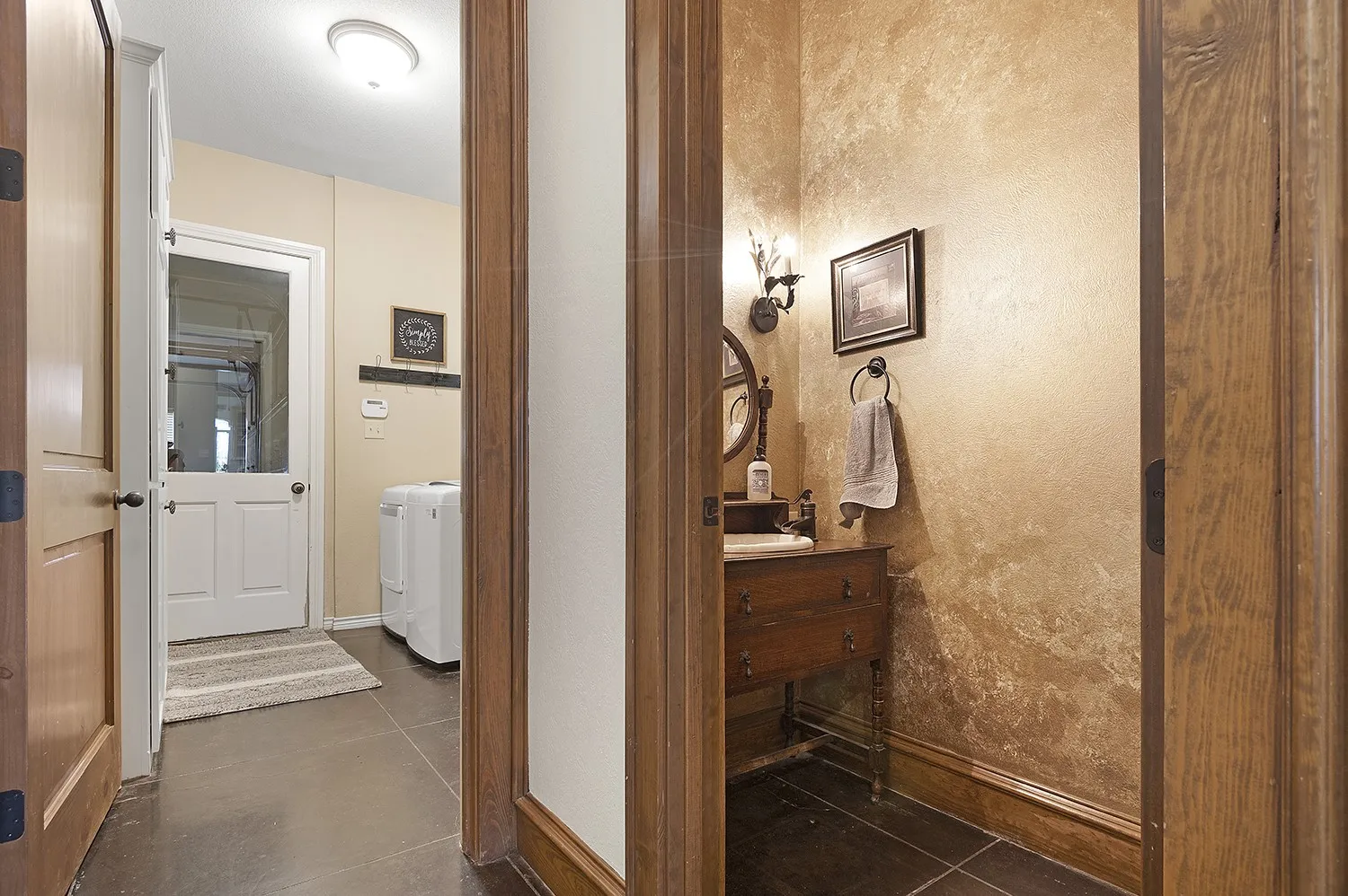 Hallway with dark tile flooring, leading to a utility room with a white exterior door featuring a glass panel